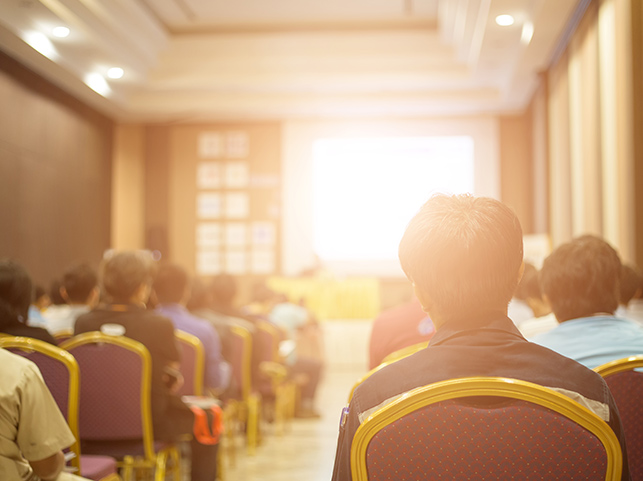 Back view of an audience seated in a seminar or conference room, focused on a presentation.