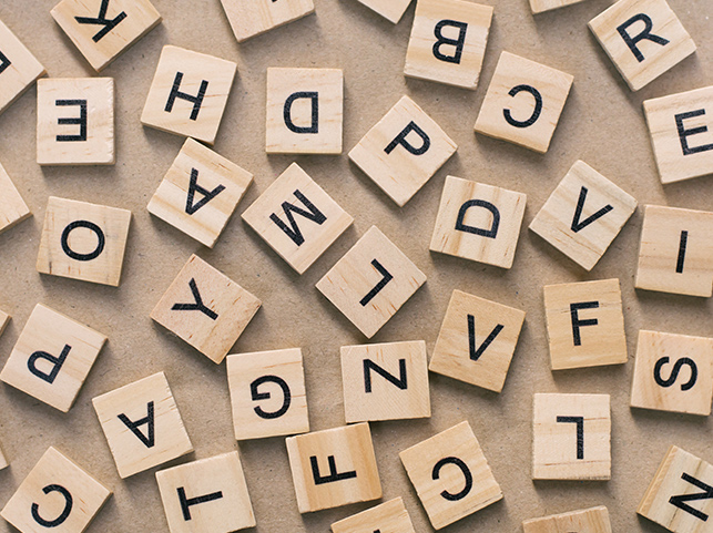 Scattered wooden tiles displaying various letters on a textured background.