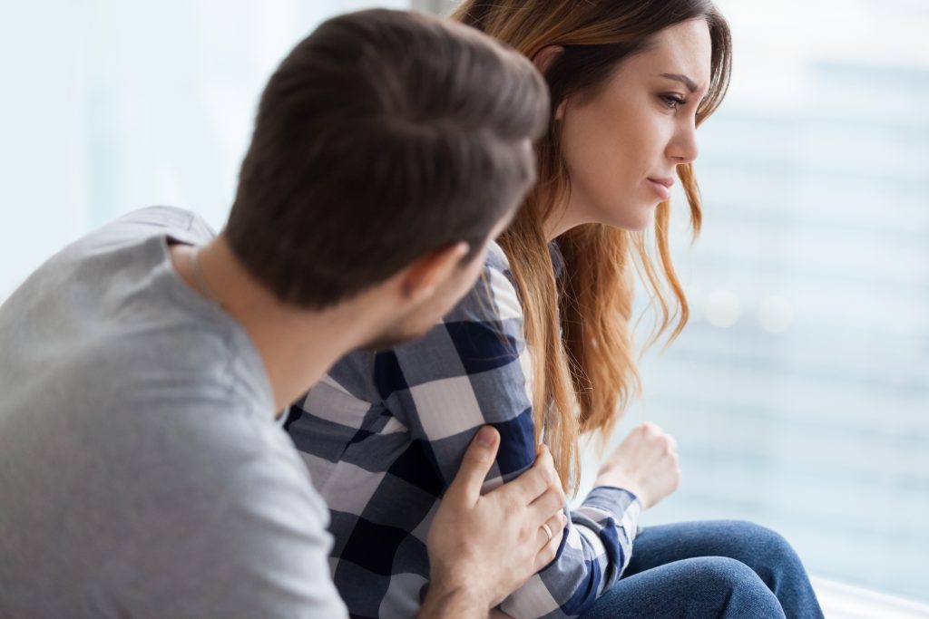 Man comforting an upset woman, with arms around her.