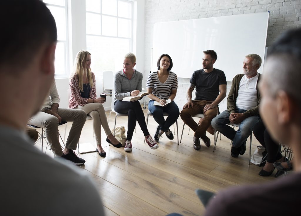 A group sitting at desks in a circle in a classroom discussing.