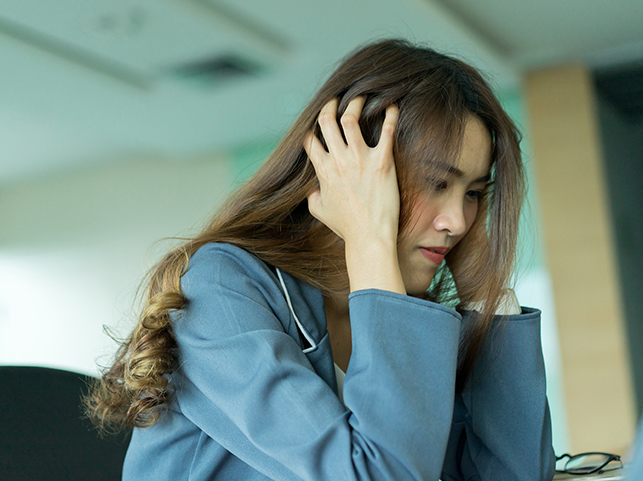 A young woman in a blue blazer with her hand running through her hair, deep in thought.