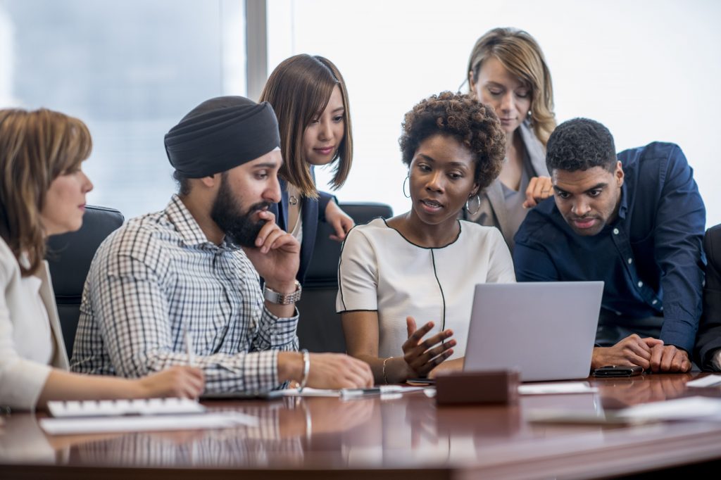 Group of people gathered around a computer at a desk discussing.