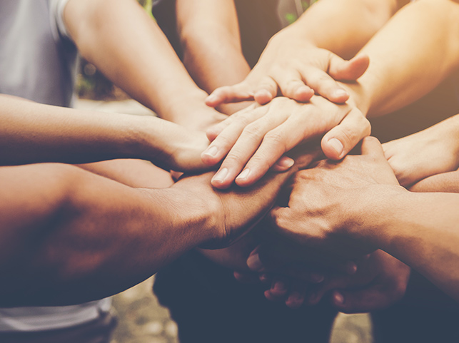 Multiple hands of diverse individuals joined together in a circle, symbolizing unity and support